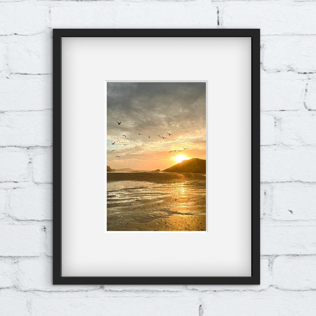 Framed artwork of a sunset over water with birds on a white brick wall.