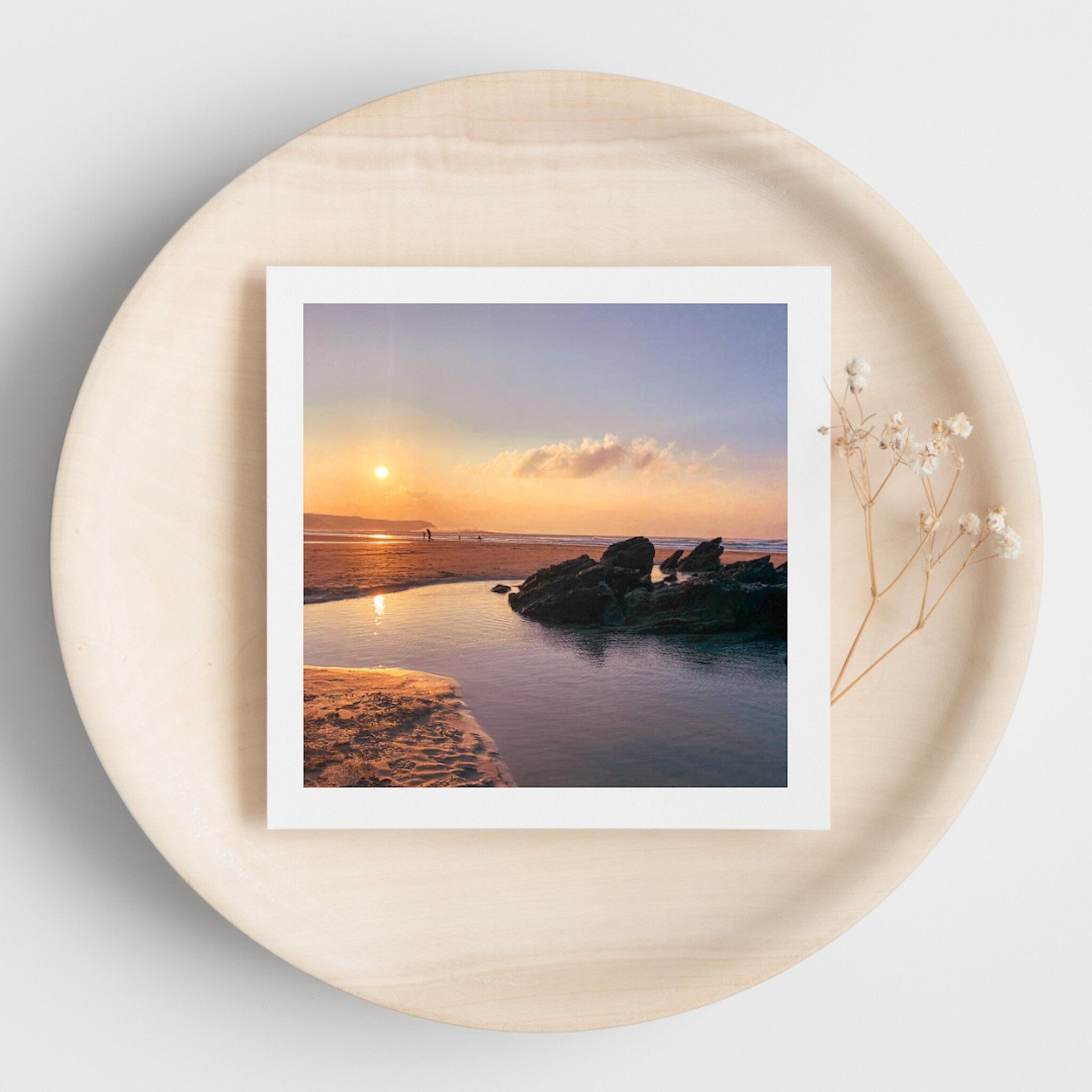Framed photograph of a sunset over a beach with rocks  and rock pools on a beige plate.