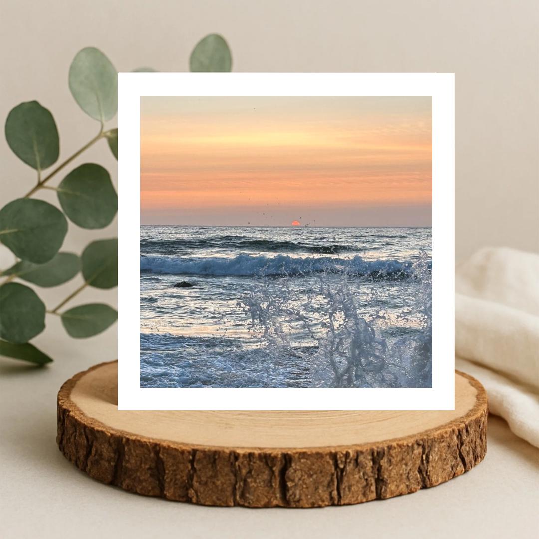 Sunset over the ocean with splashing wave, greetings card on a wooden coaster