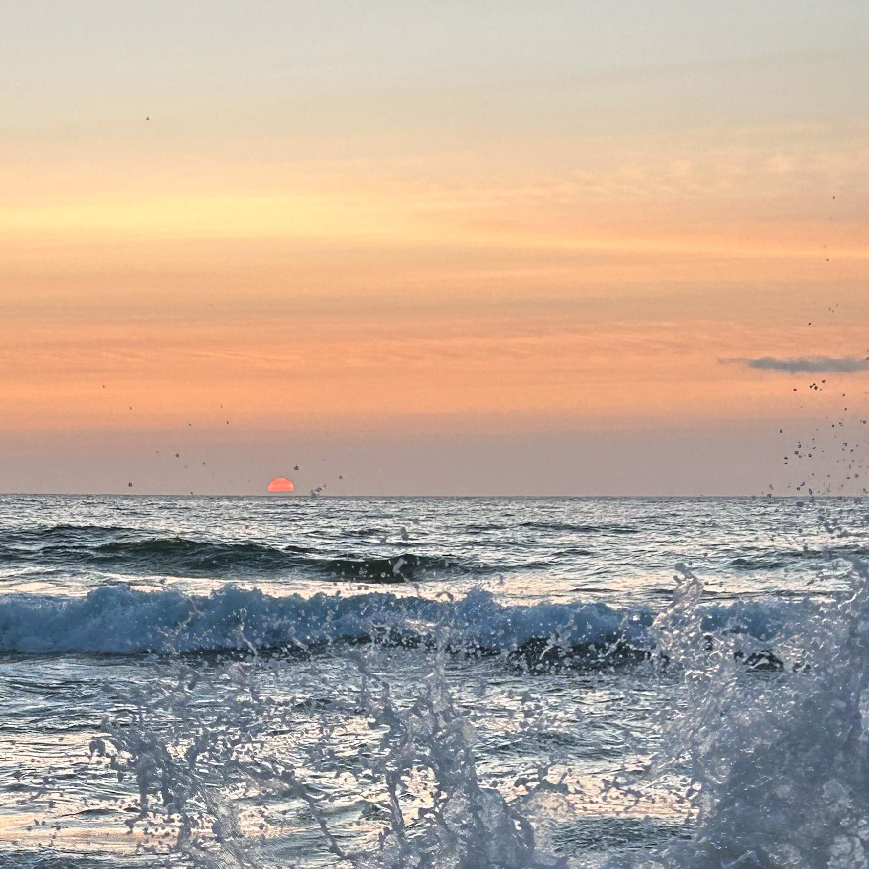 Sunset over the ocean with waves crashing on the shore
