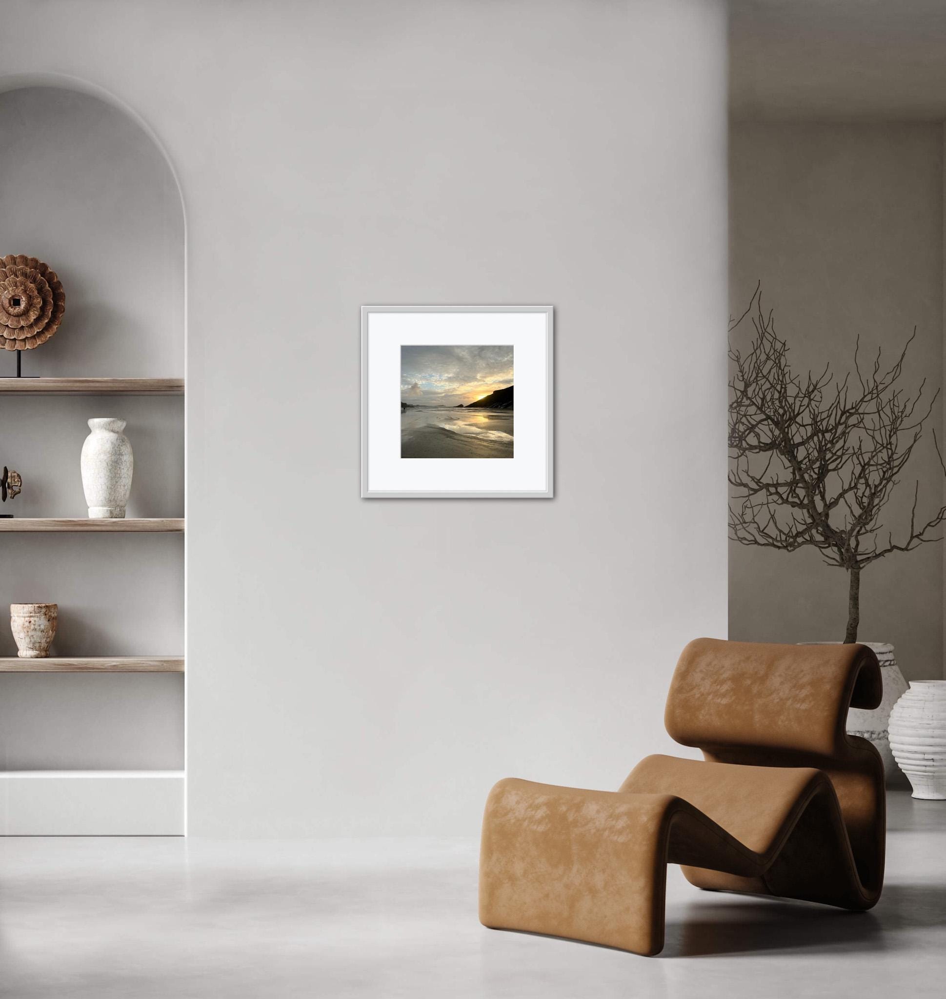 Framed sunset artwork on a wall with a modern chair and shelves in the foreground