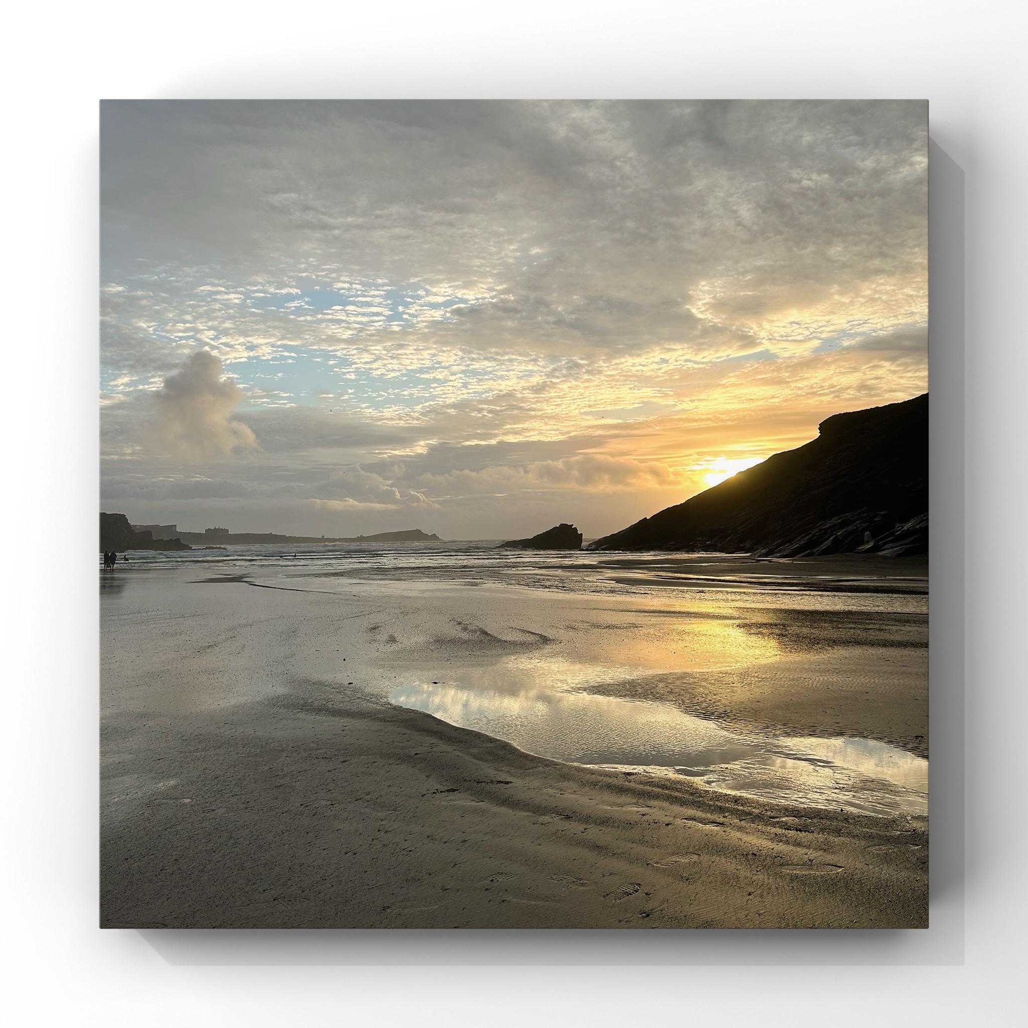 Beach scene with sunset reflected in wet sand and silhouetted headland.