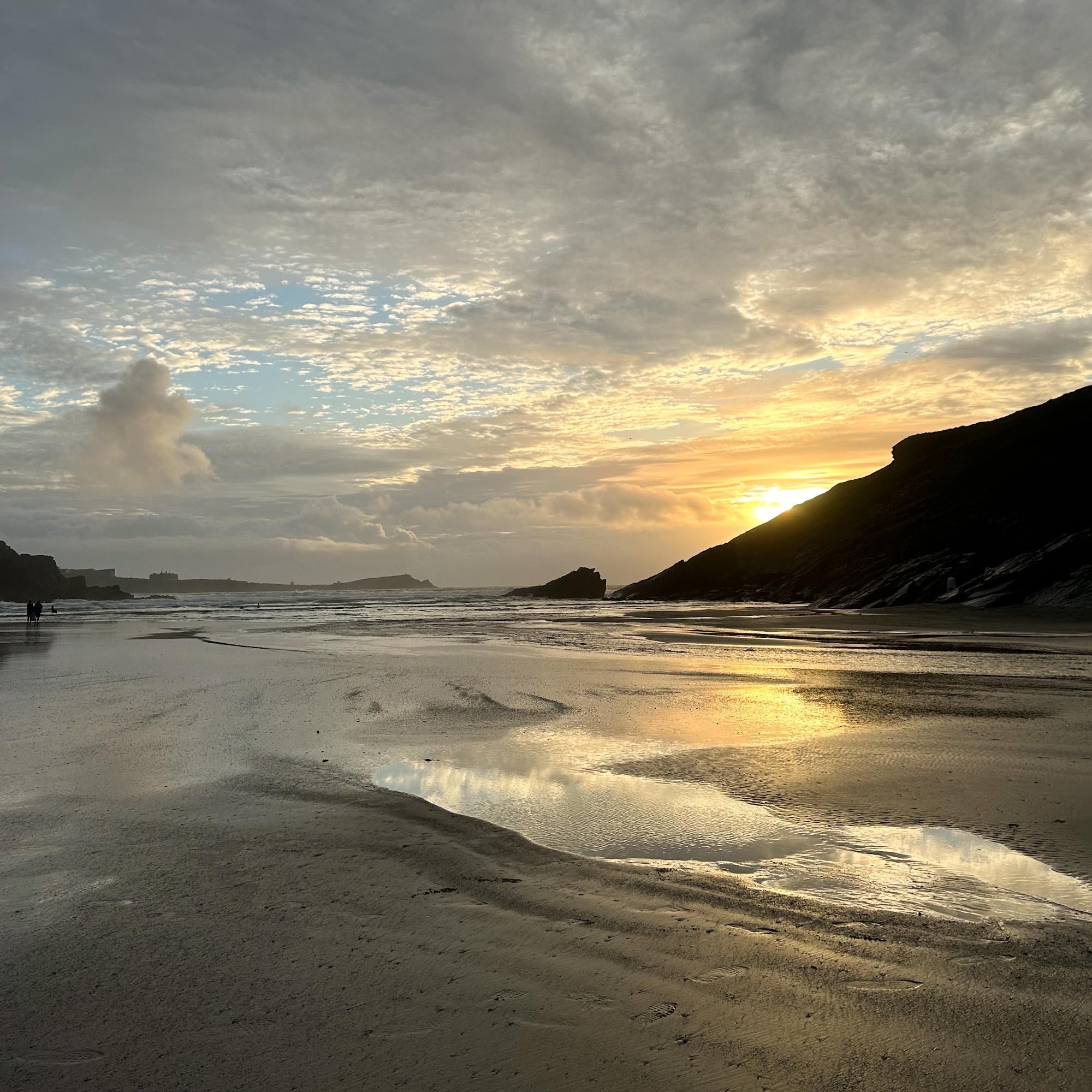 Beach scene with sunset reflected in wet sand and silhouetted headland
