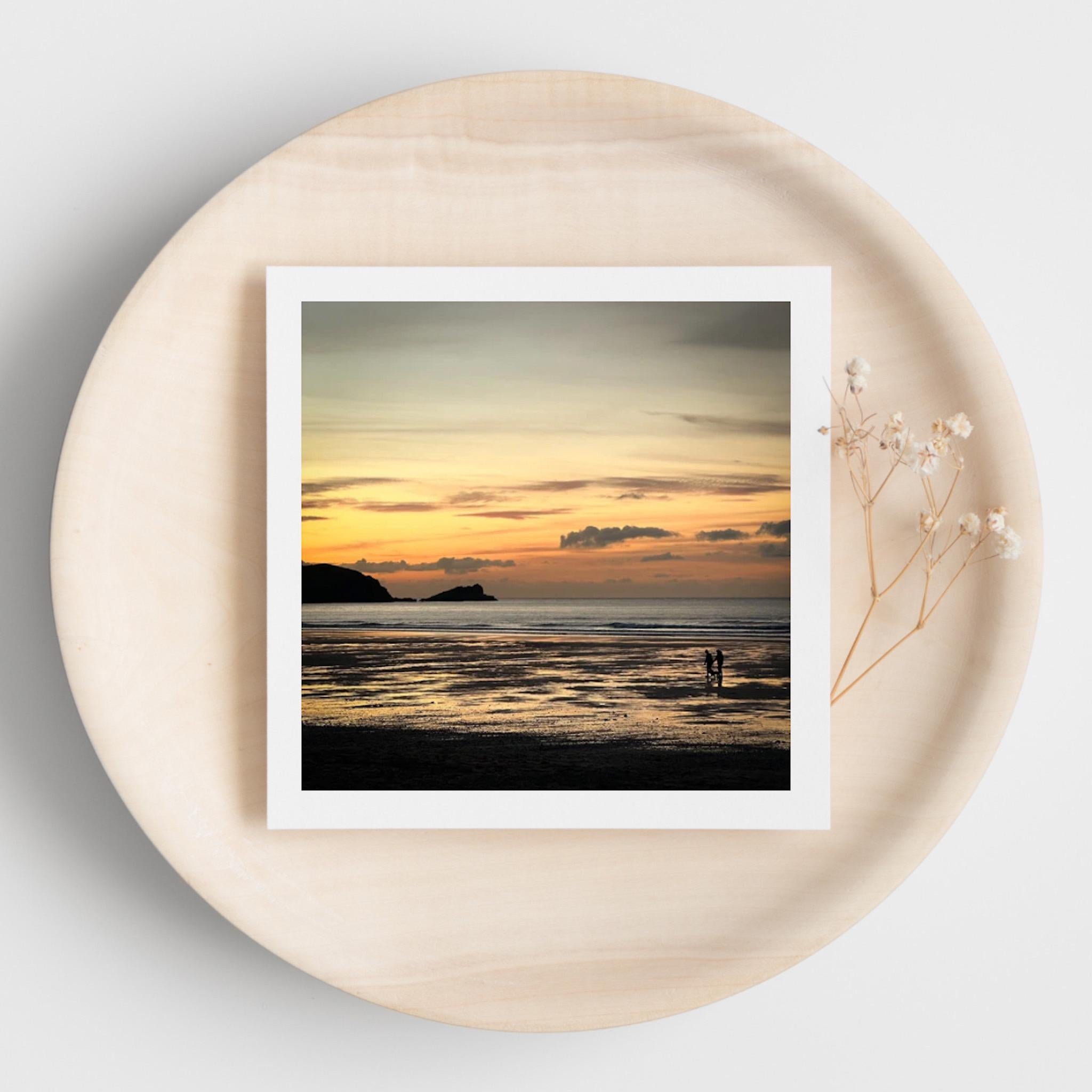 Square greetings card with a photograph of a sunset over water on a round beige surface.