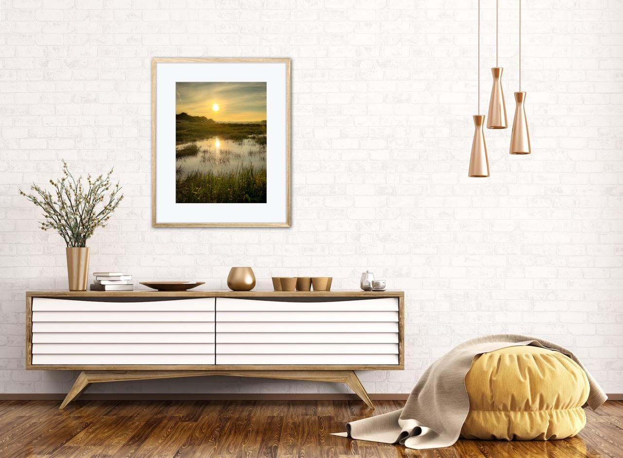Modern living room with a wooden console table, framed marsh estuary sunrise artwork, and decorative items.