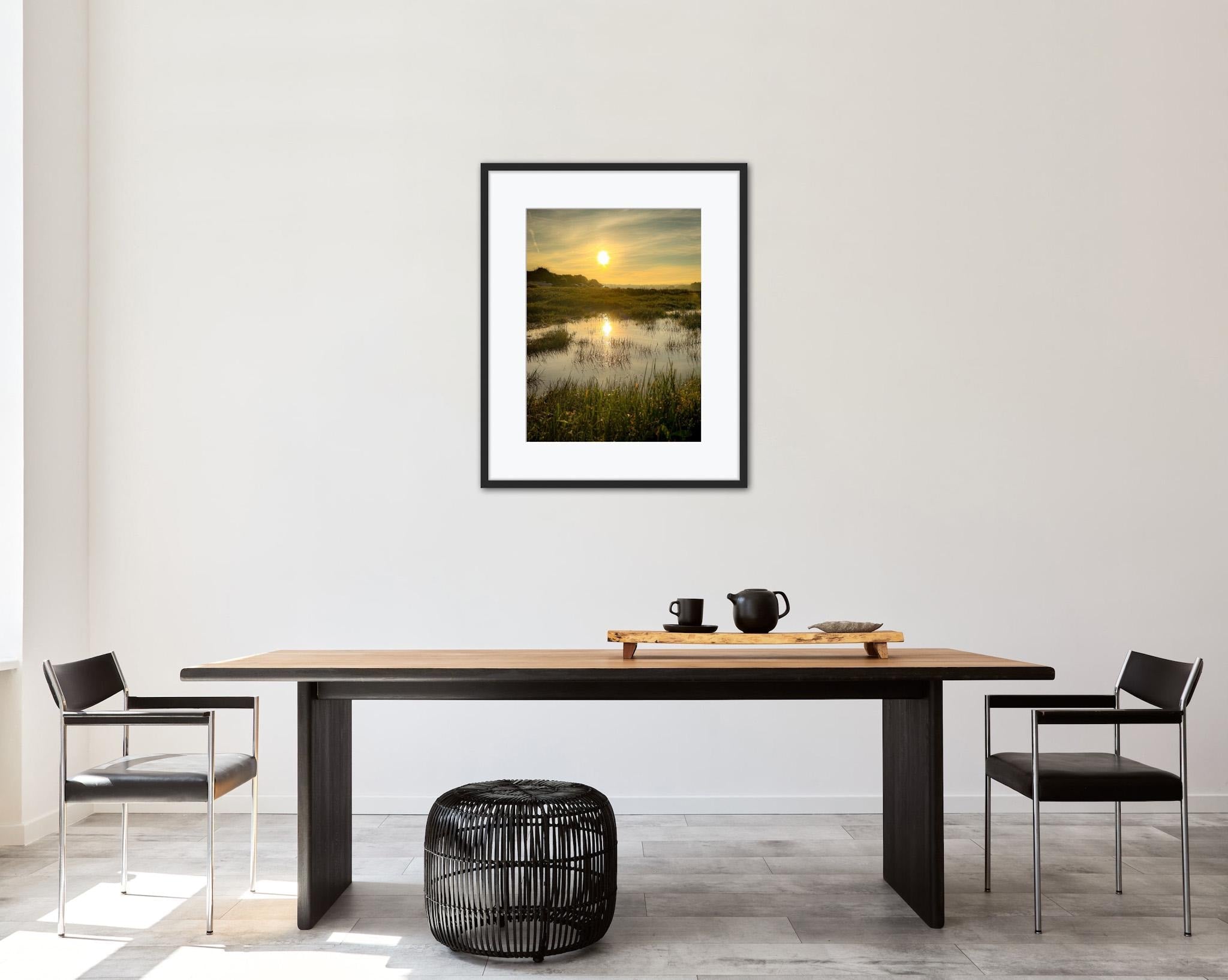 Dining room with a wooden table, chairs, and a framed landscape print of a marsh at sunrise on the wall.