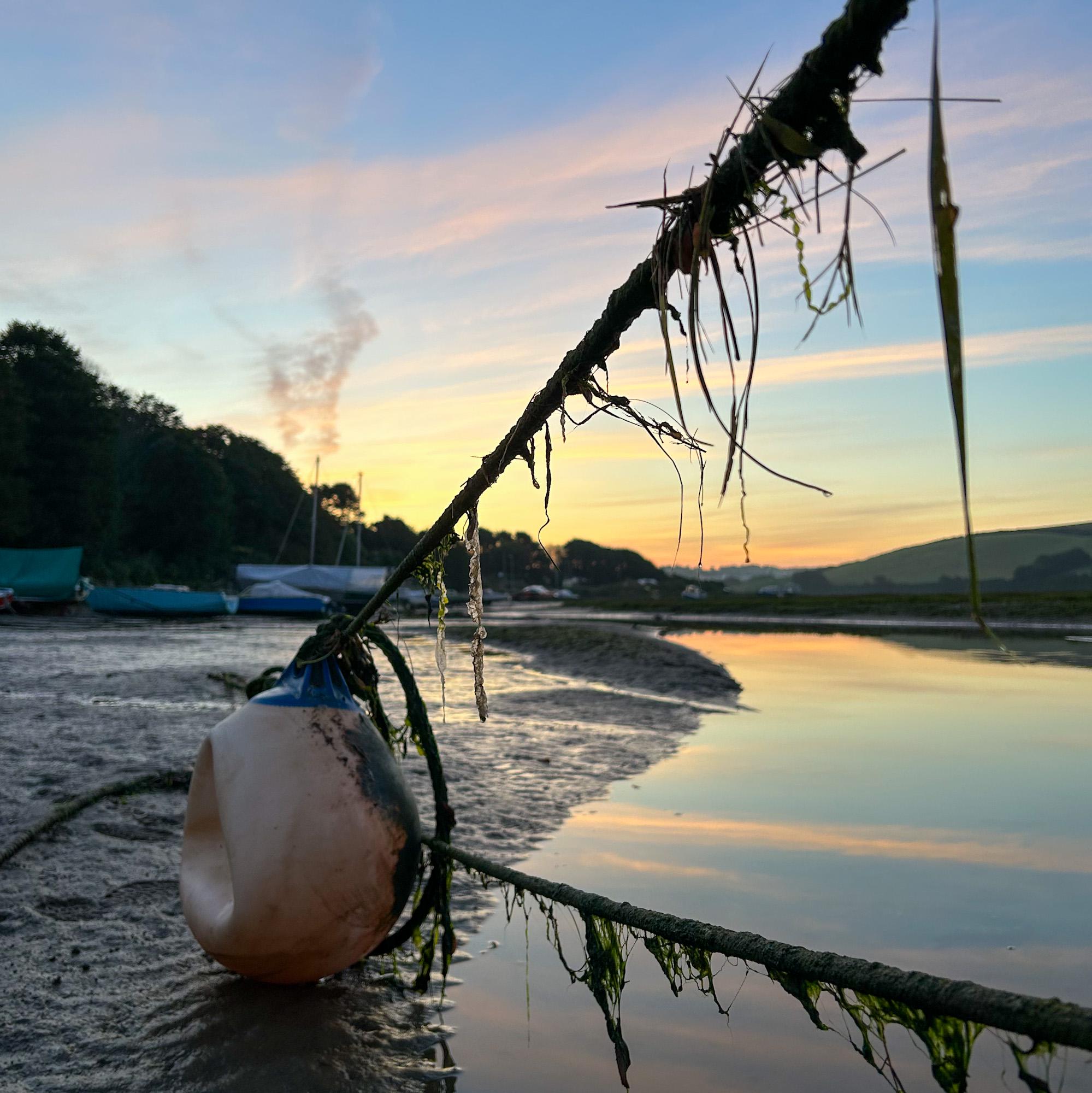 Buoy attached to a rope on a beach with a sunrise sky and boats in the background