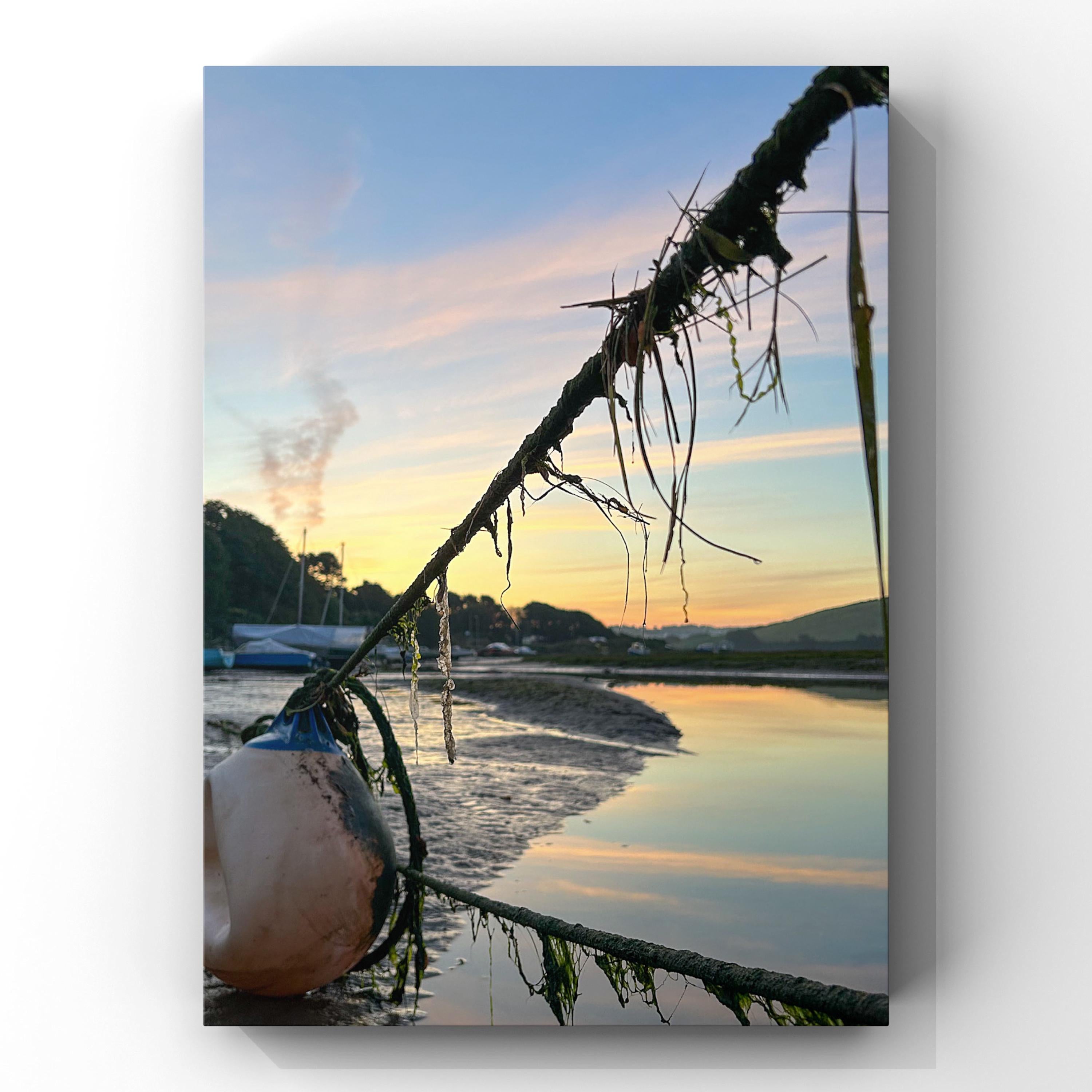 Sunrise over a calm body of water with mooring ropes and buoy in the foreground.