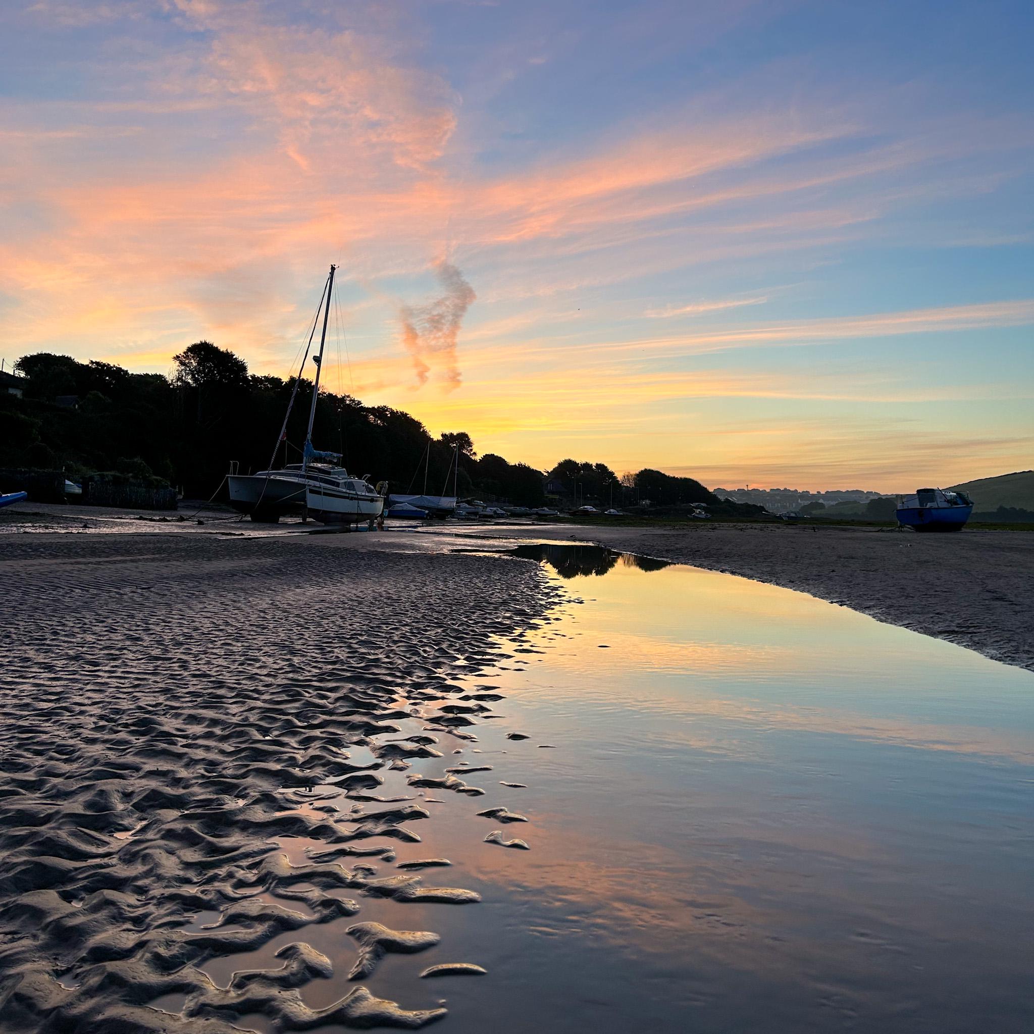Beach scene with boats at sunrise, reflecting on water