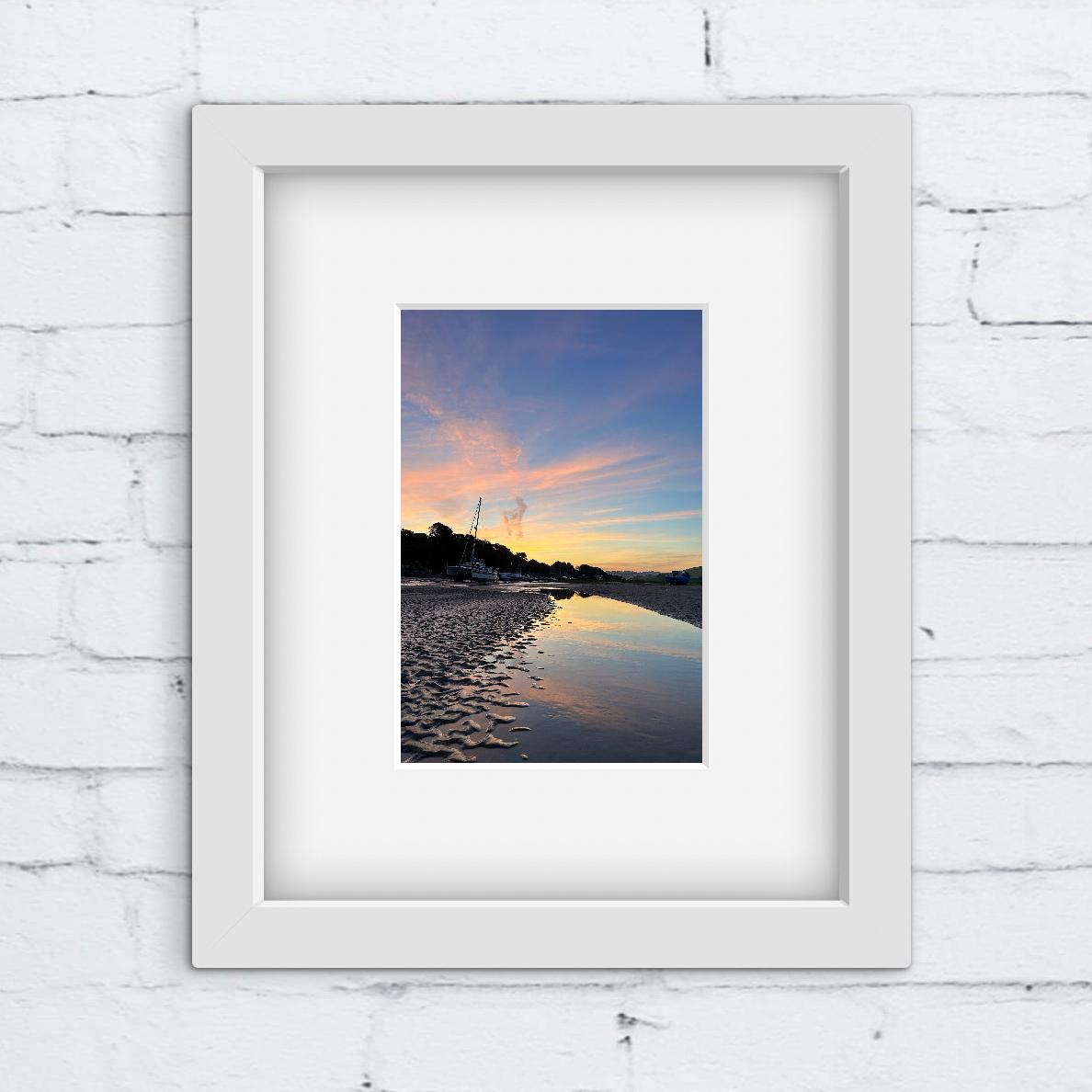 Framed photograph of a beach sunset on a white brick wall