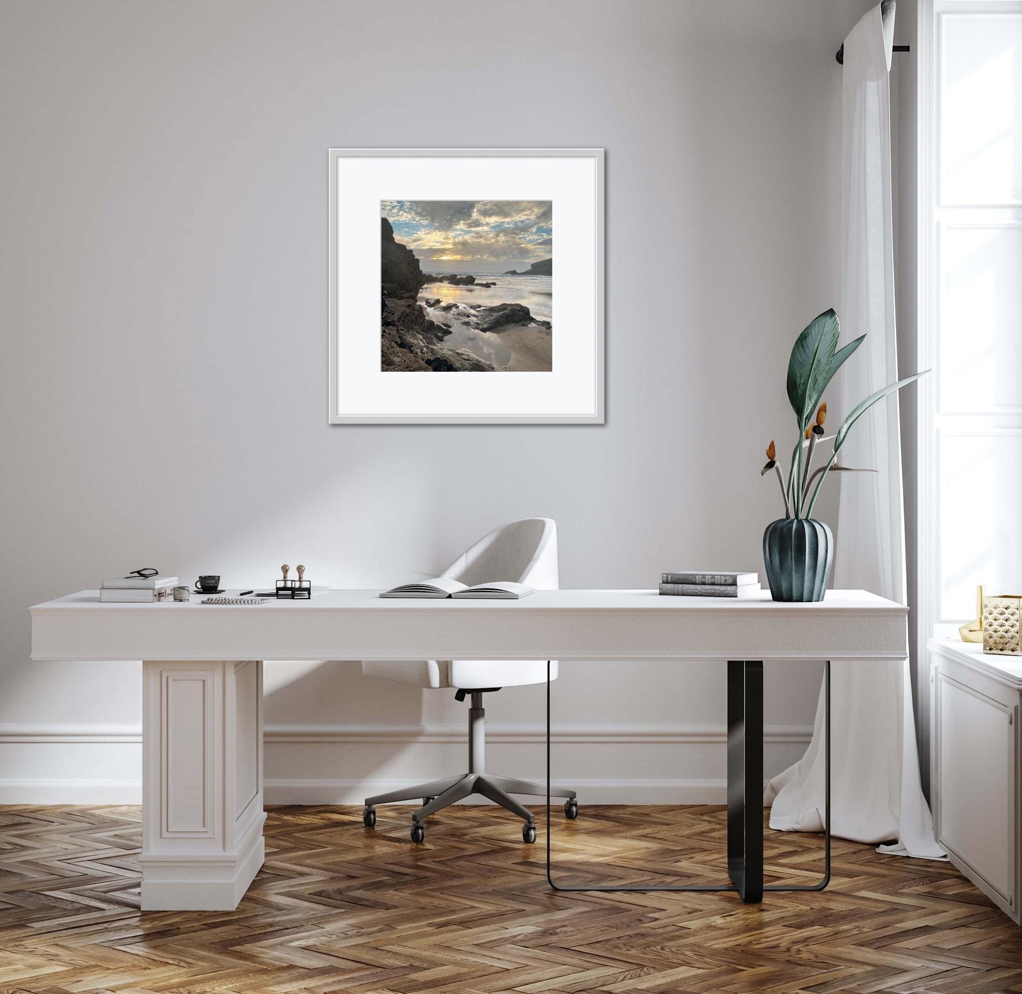 Modern office setup with a desk, chair, and framed sunset on a rocky shore artwork on a wall.