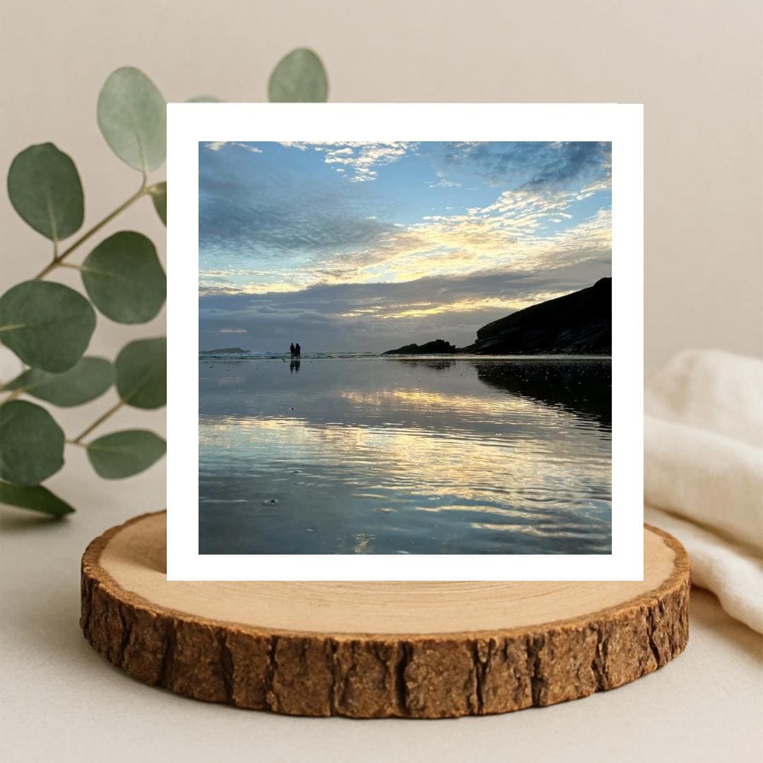 Scenic view of a beach with people standing in the water, greetings card on a wooden log slice.