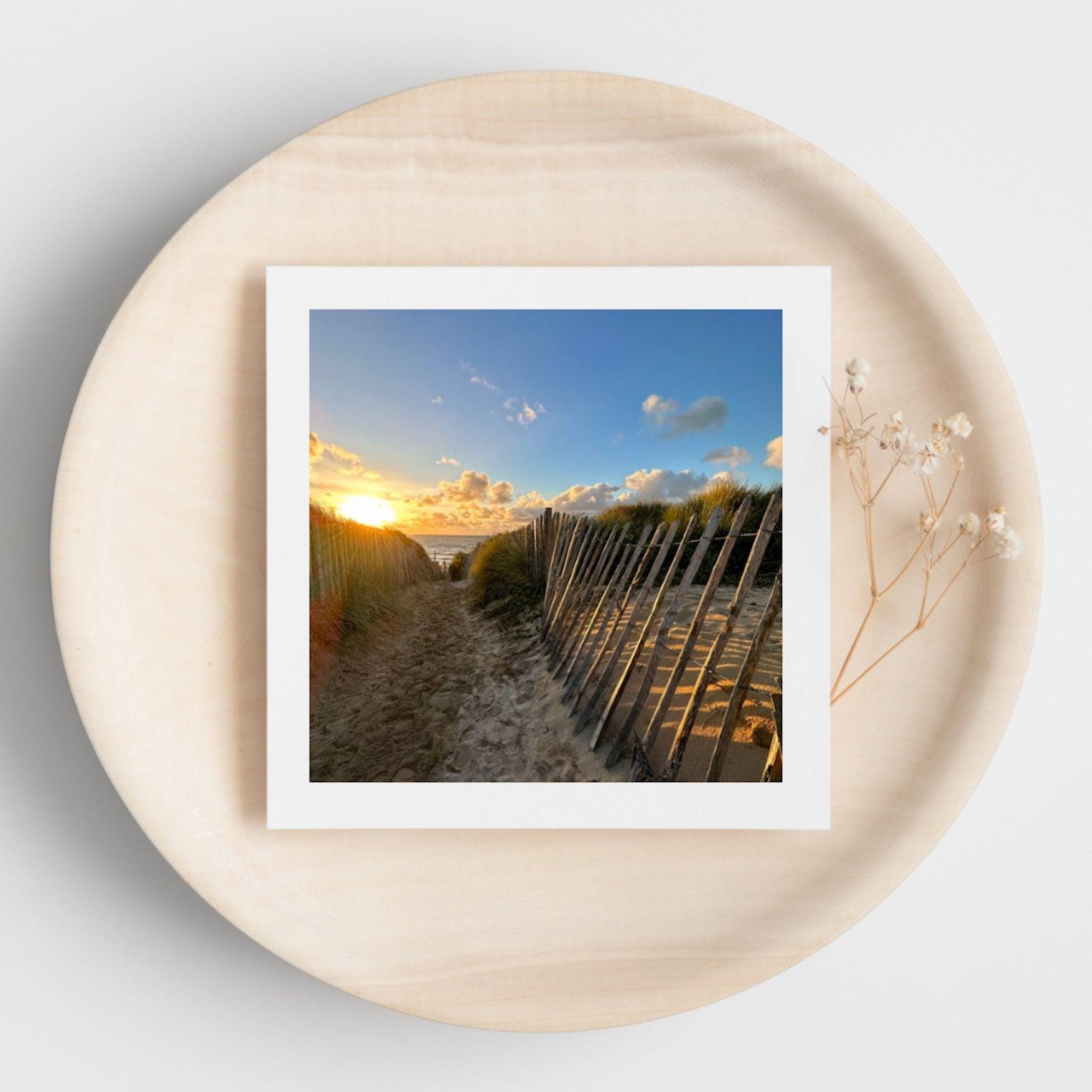 Greetings card with photograph of a beach scene with sunset and wooden walkway. Displayed on a beige plate.