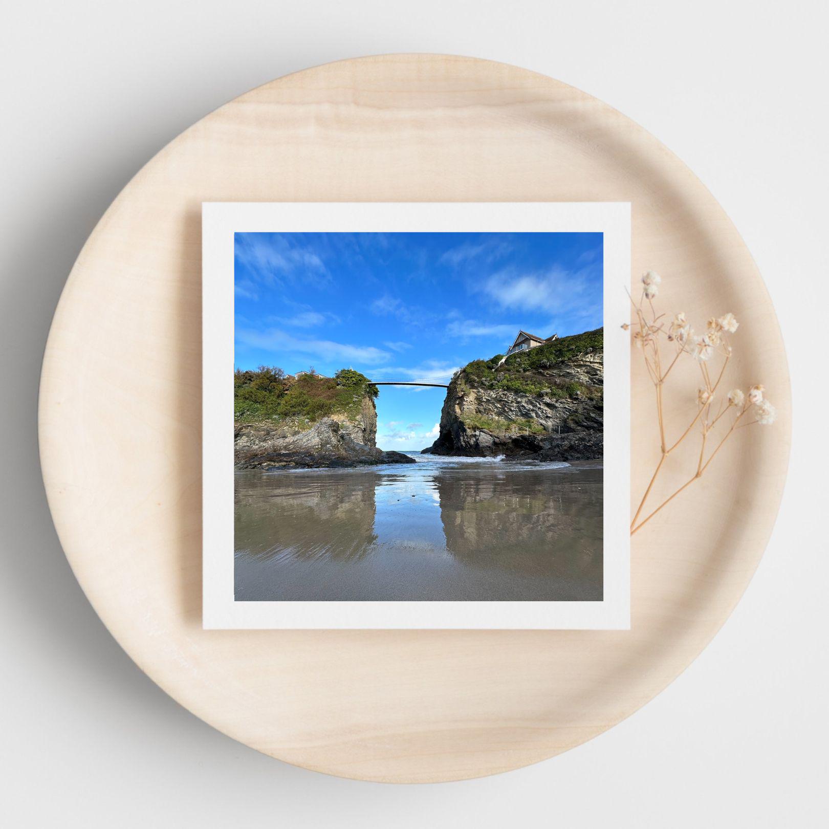 White bordered photograph of a coastal landscape with a clear blue sky on a greetings card displayed on a beige plate.