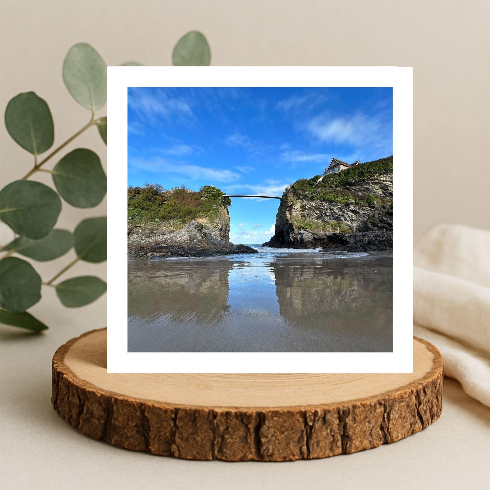 Card with a scenic view of a coastal landscape with a bridge over water, displayed on a wooden stand.