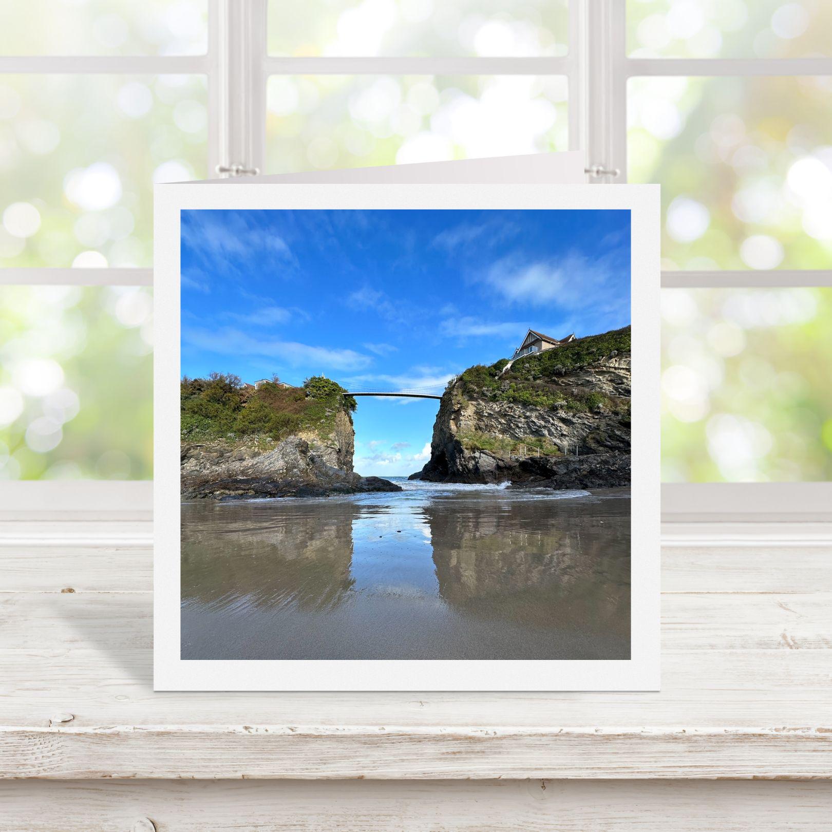 White bordered photograph of a coastal scene with a bridge and cliffs on a square greetings card.