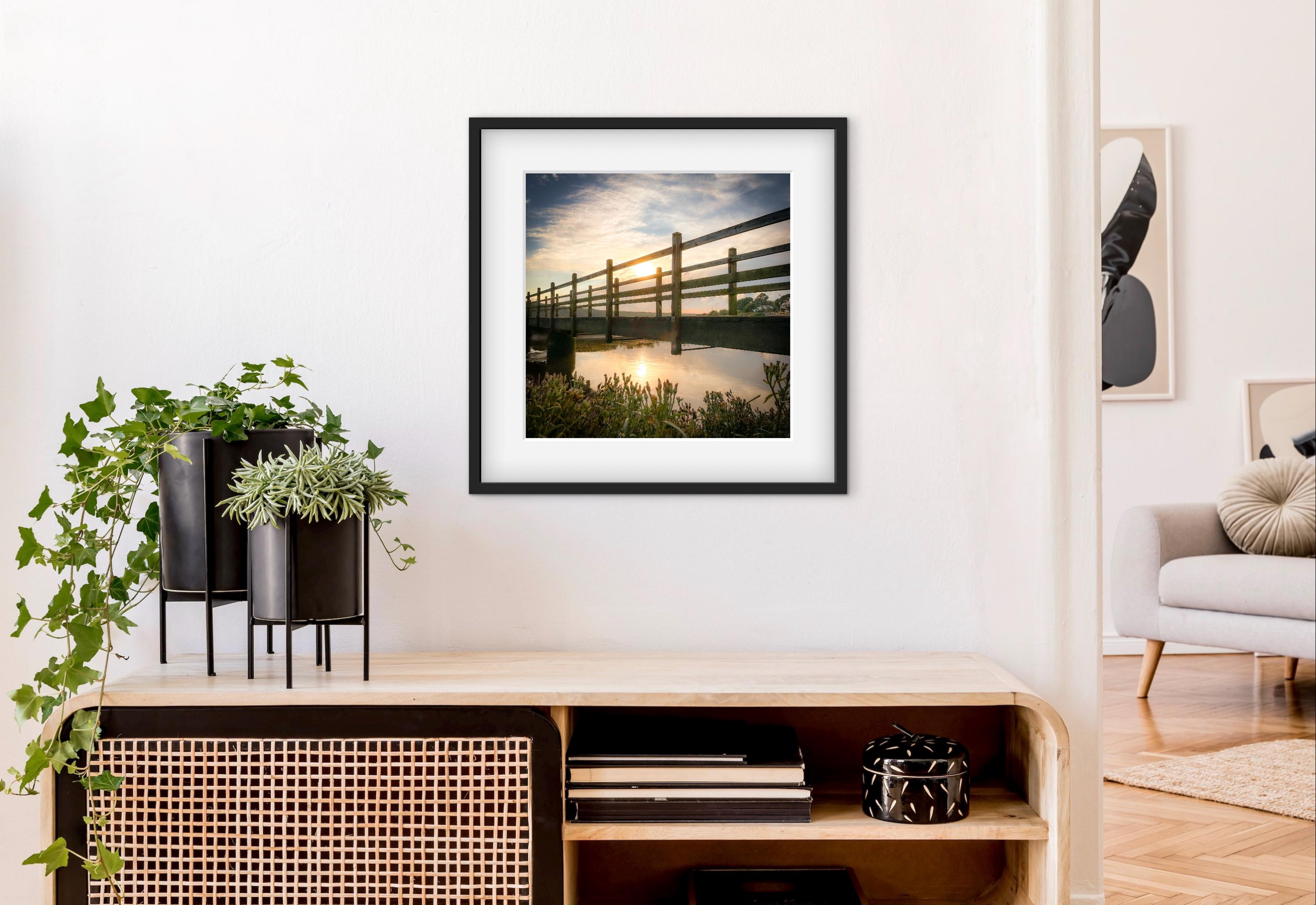 Framed photograph of a sunset over a wooden bridge in a modern living room.
