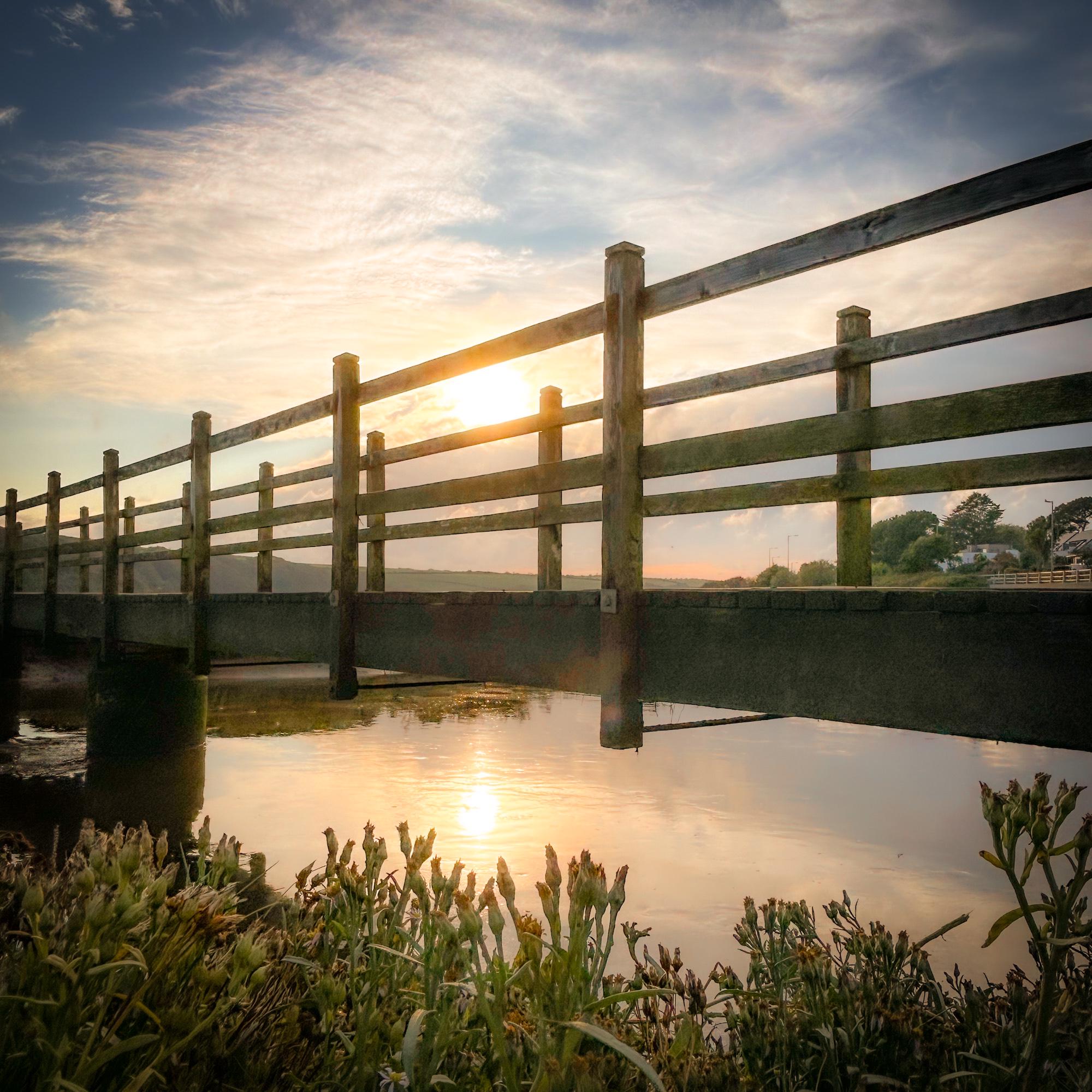 Wooden bridge over a body of water with a sunset in the background