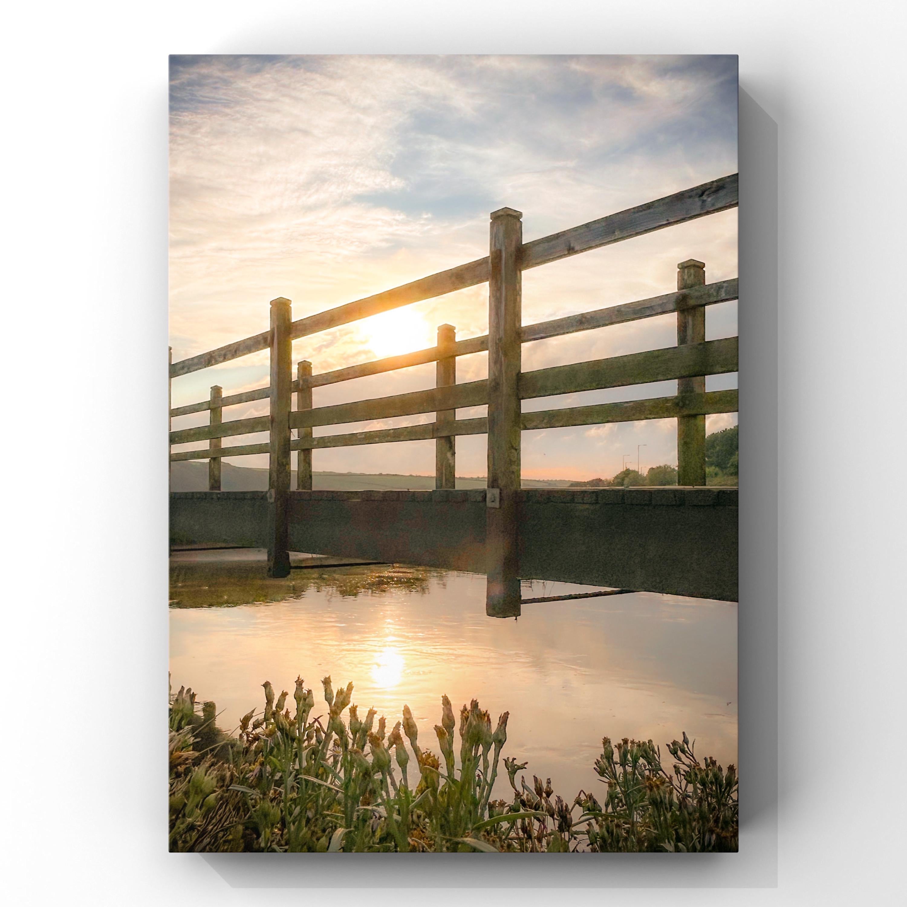 Wooden bridge over a calm body of water with a sunset in the background