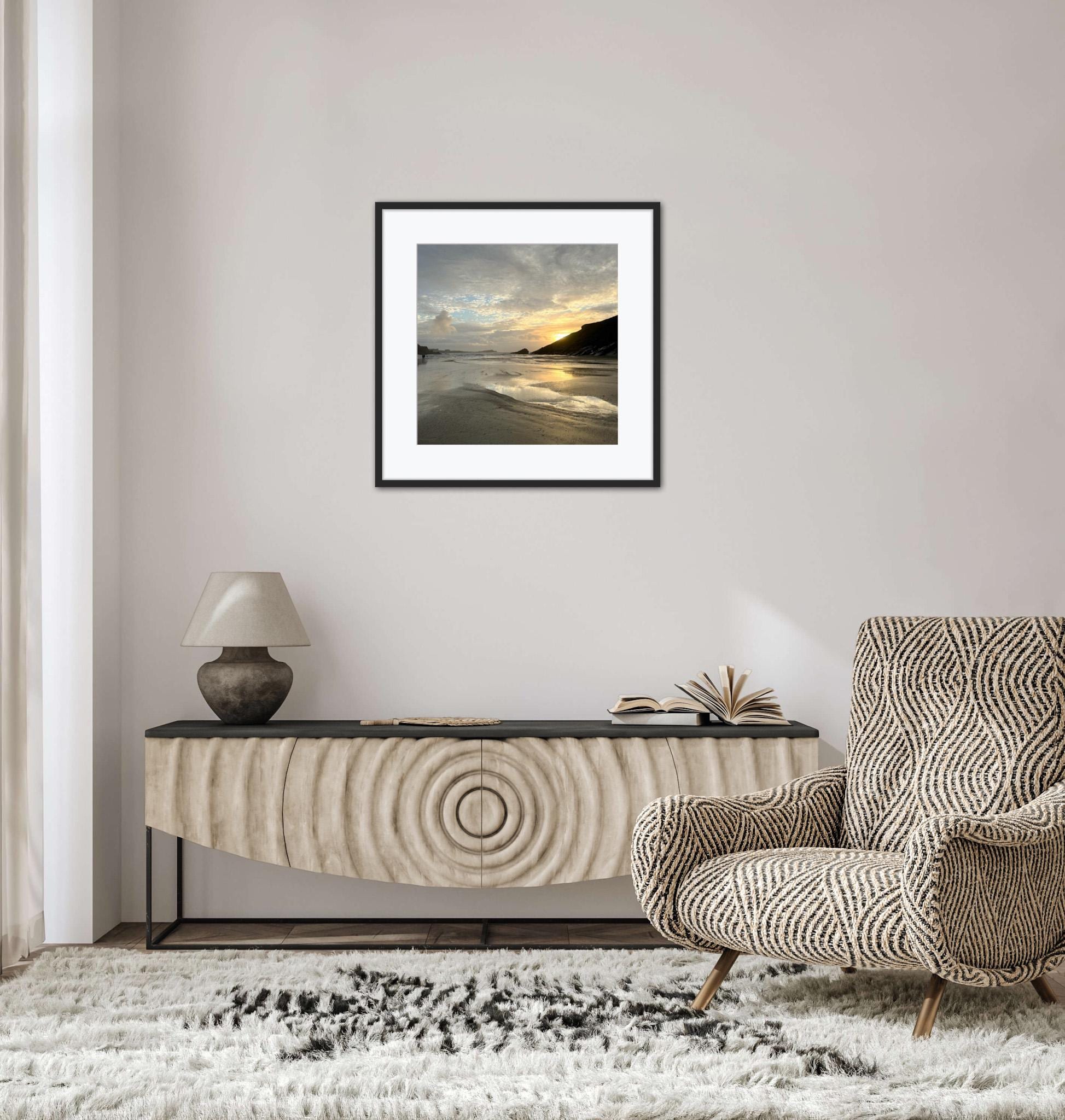 Modern living room with a framed sunset beach scene, console table, and armchair.