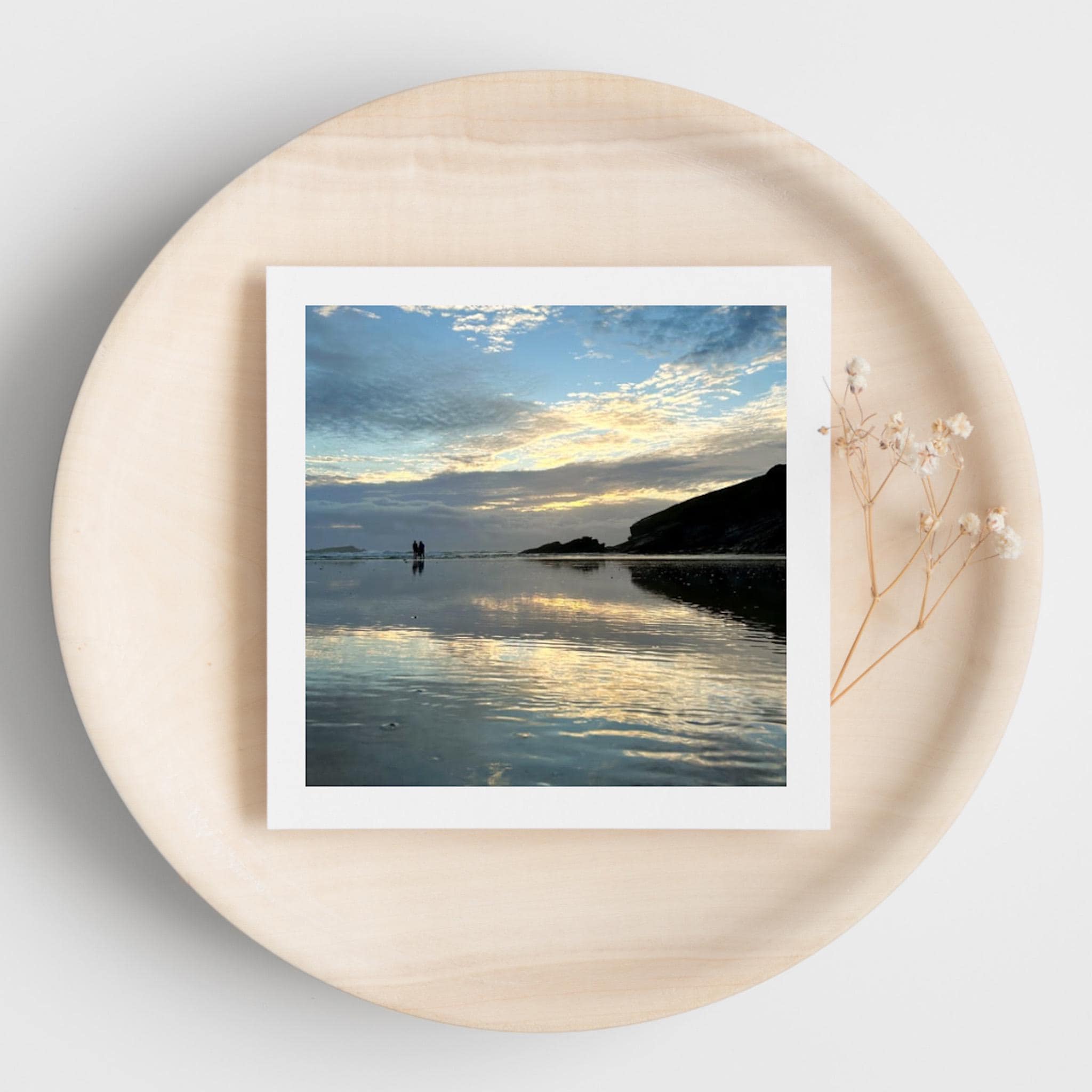 Square greetings card of a sunset reflected in wet sand on a round wooden surface.