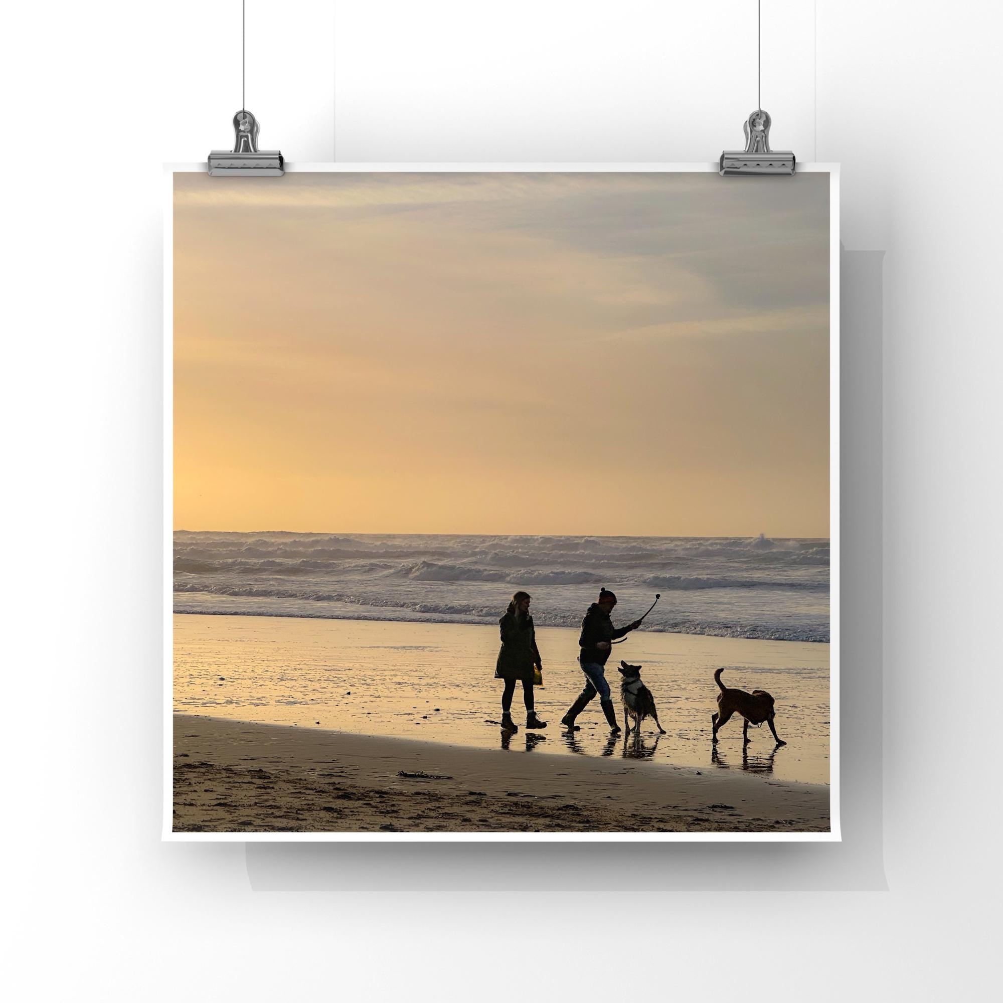 Two people and two dogs walking on a beach at sunset.