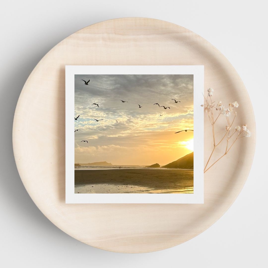 Framed beach sunset print on a round wooden surface with dried flowers.