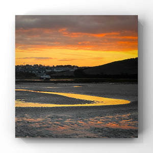 Sunrise over a coastal landscape with a bright orange sky reflected in a stream of water.