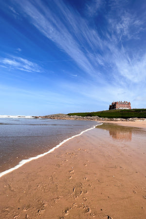 Beach scene with an old hotel on a headland under a blue sky