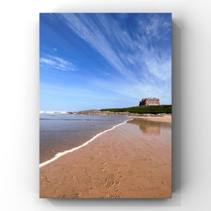 Beach scene with an old hotel on a headland under a blue sky