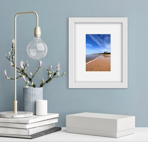 Decorative setup with a lamp, books, and framed beach photo on a light blue wall.