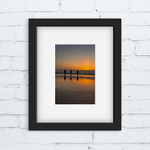 Framed photograph of a sunset on a beach with three people silhouetted against the water.