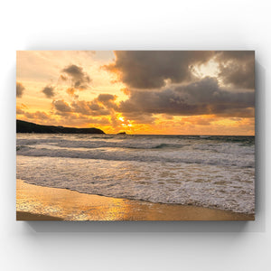 Sunset over the ocean reflected in the wet sand with waves crashing onto a beach 