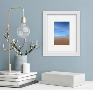 Decorative setup with a lamp, books, and framed beach and blue sky picture on a light blue wall.