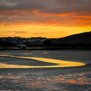 Orange sunrise over a coastal landscape with a small settlement and winding orange river.