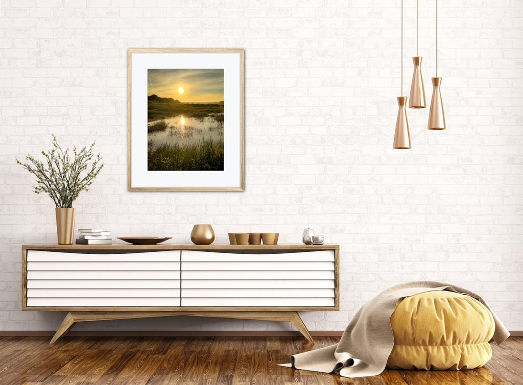 Modern living room with a wooden console table, framed marsh estuary sunrise artwork, and decorative items.