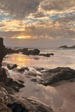 Sunset over a rocky beach with water reflecting the colors of the sky.