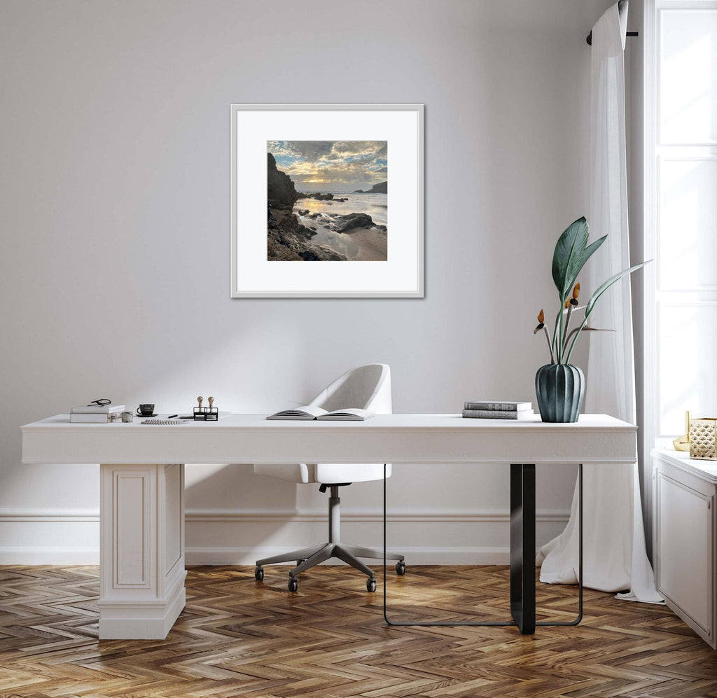 Modern office setup with a desk, chair, and framed sunset on a rocky shore artwork on a wall.