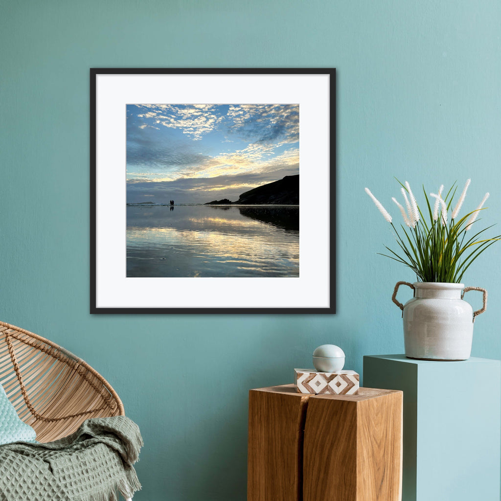 Framed artwork of a beach scene  at sunset reflected in wet sand on a teal wall with a chair and decorative items.