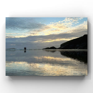 Two people standing on a beach with a reflective water surface and a dramatic sky.