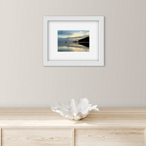 Framed photograph of a scenic reflected sunset landscape on a wall above a wooden surface with a decorative bowl.