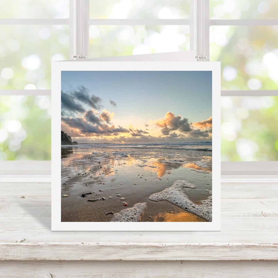 White edged beach sunset print on a greetings card displayed on a wooden surface with a window in the background