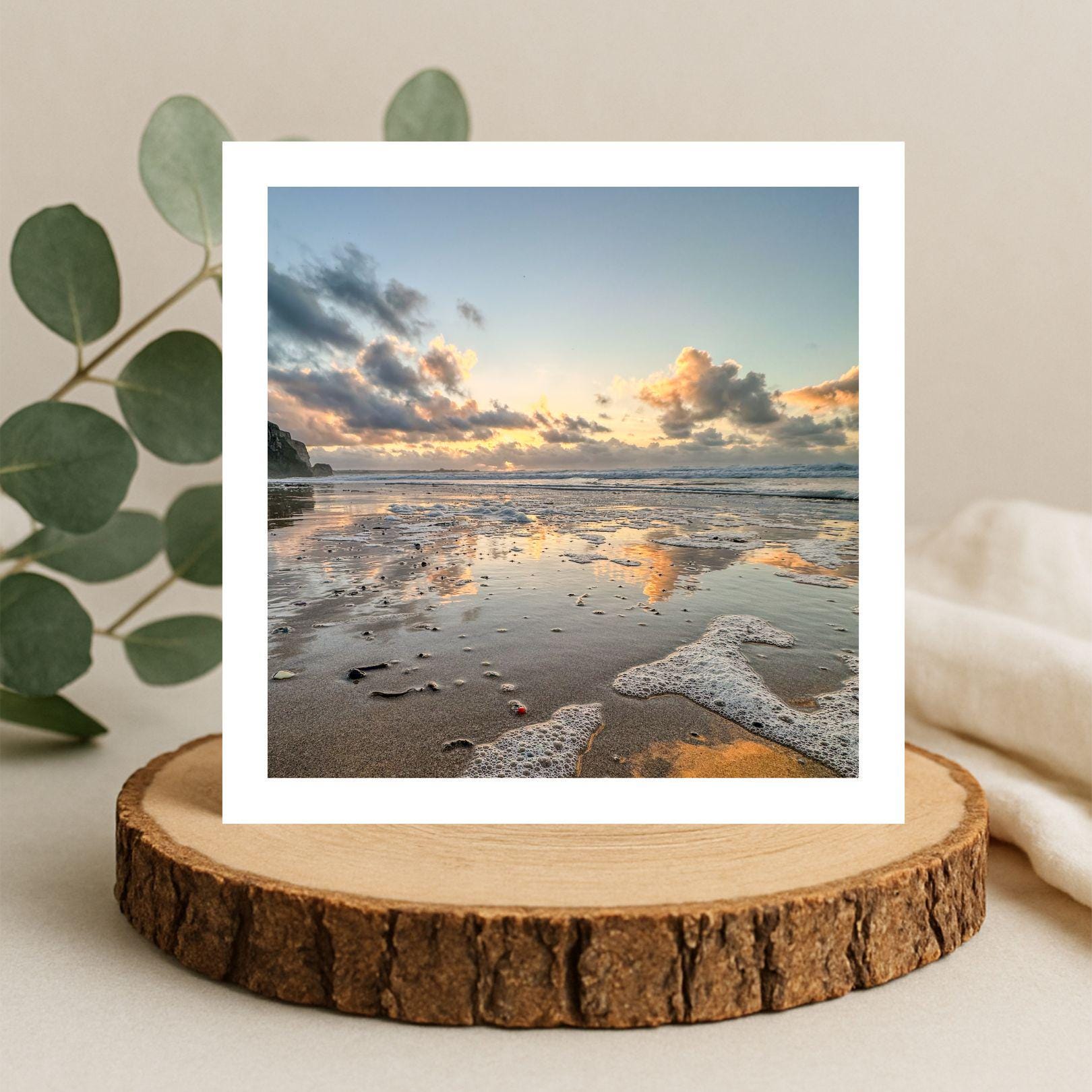 Greetings card withbeach photograph of clouds reflected in wet sand at sunset. On a wooden stand with decorative elements.