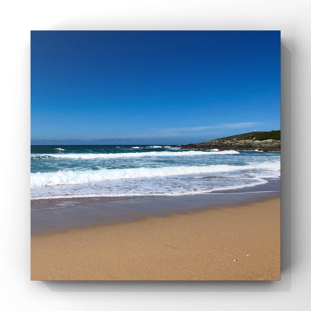 Beach scene with waves crashing onto the shore under a clear blue sky.