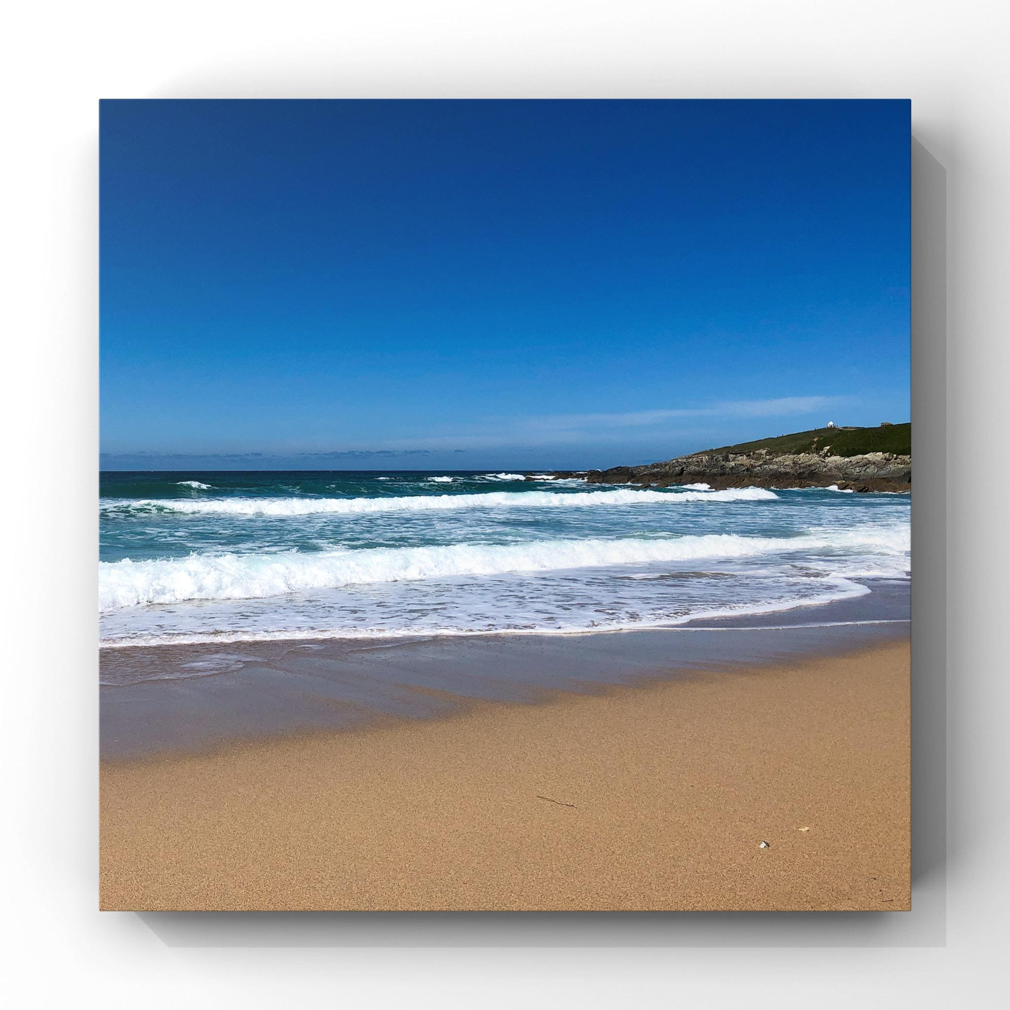 Beach scene with waves crashing onto the shore under a clear blue sky.