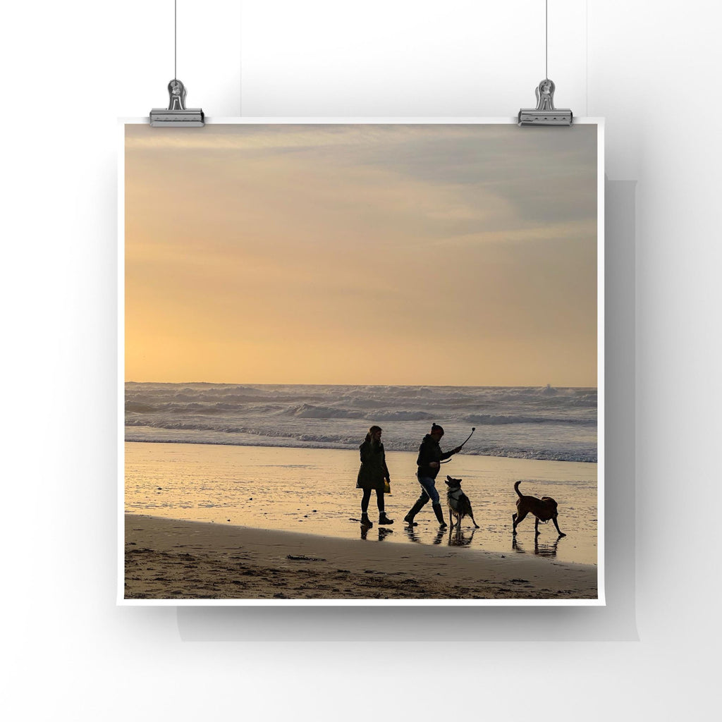 Two people and two dogs walking on a beach at sunset.